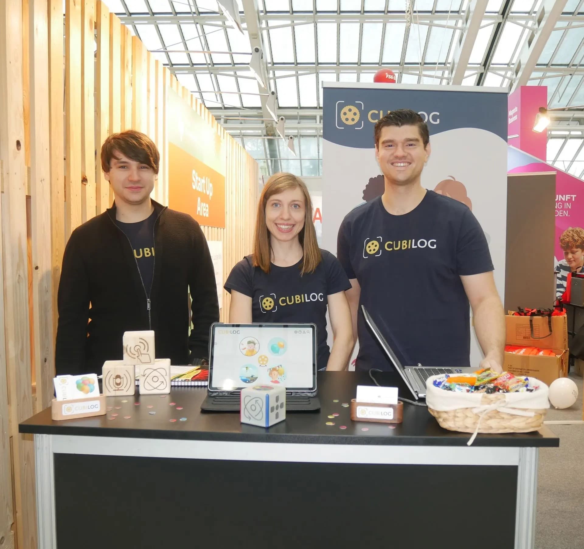 Das Cubilog-Team – Daniel, Carina und Andreas – steht an ihrem Stand im Start-up-Bereich einer Messe und präsentiert ihre hölzernen Lernwürfel und die dazugehörige App.
